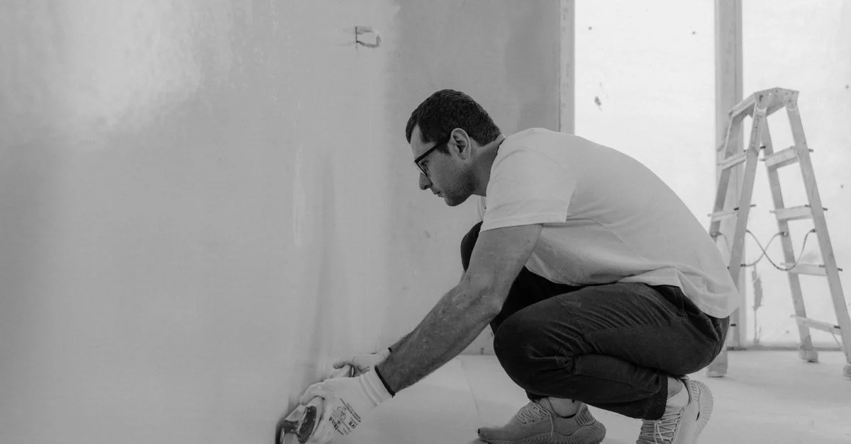 Image monochrome d'un homme rénovant un mur intérieur avec des outils à plâtre.