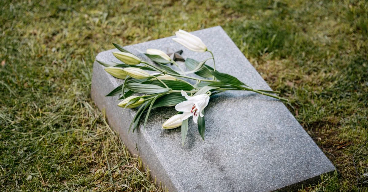 Des lys blancs placés sur une pierre tombale dans un cadre de cimetière serein.