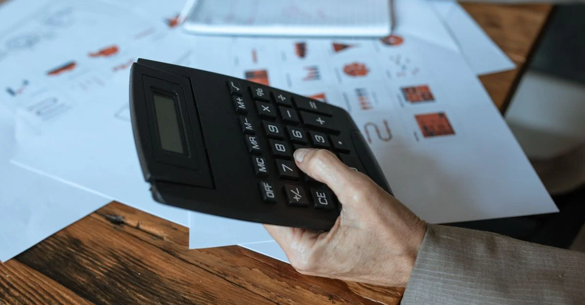 Gros plan d'une main utilisant une calculatrice sur un bureau en bois avec des graphiques.