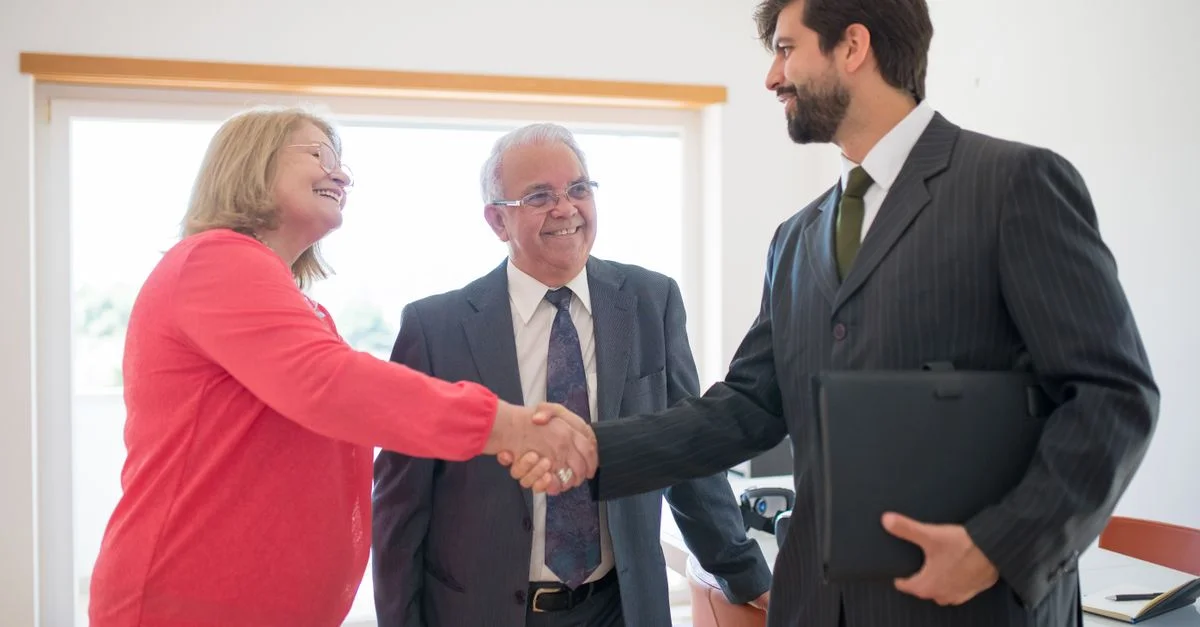Un couple senior rencontre un agent immobilier à l'intérieur, se serrant la main pour finaliser un accord de maison.