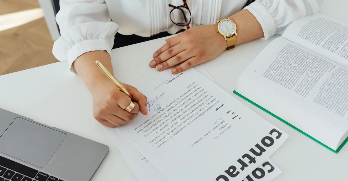 Gros plan d'une femme d'affaires signant un contrat à son bureau, avec un ordinateur portable et un livre.