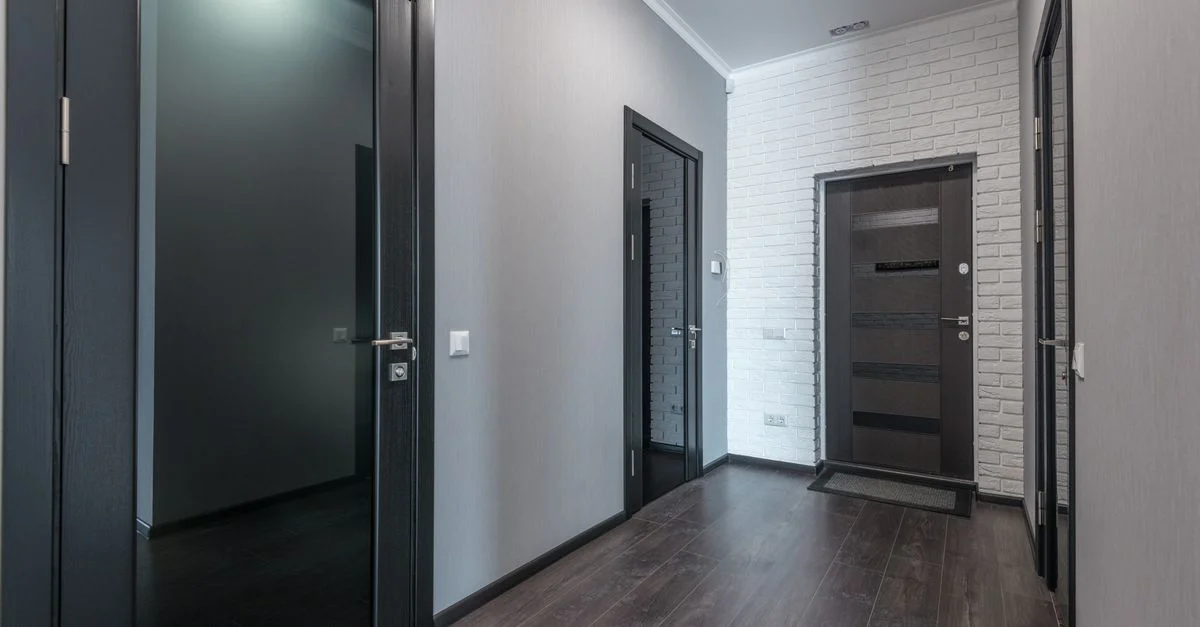 Un couloir d'appartement moderne épuré et minimaliste avec des sols en bois foncé et des portes noires élégantes.