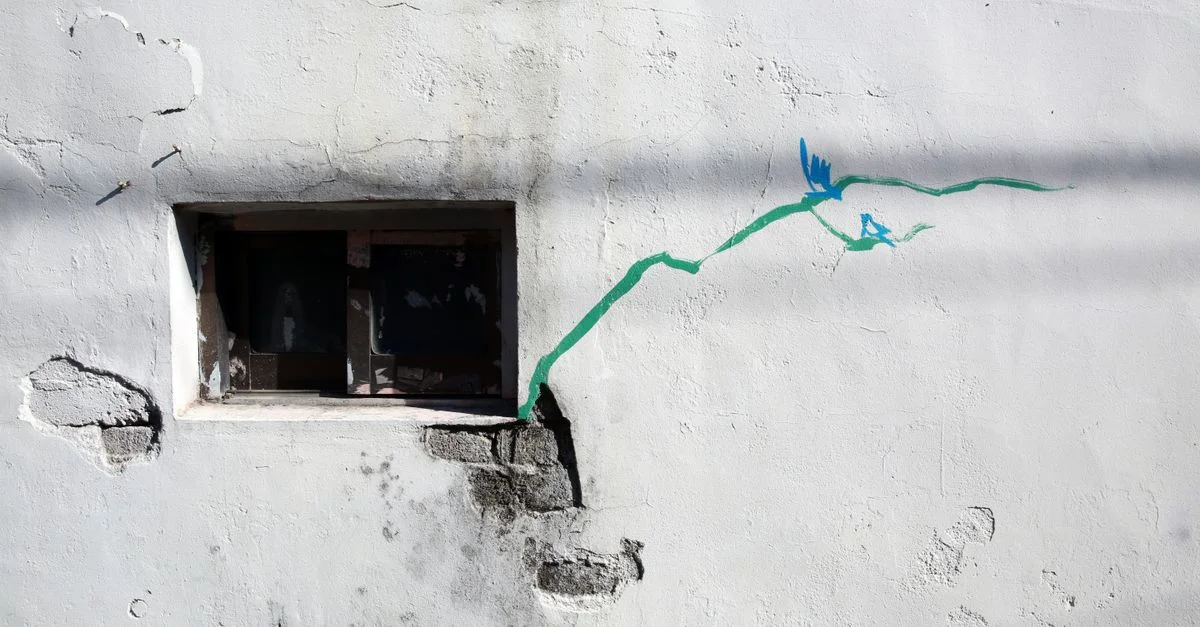 Un mur patiné avec une fenêtre, des fissures artistiques et des accents de peinture verte.