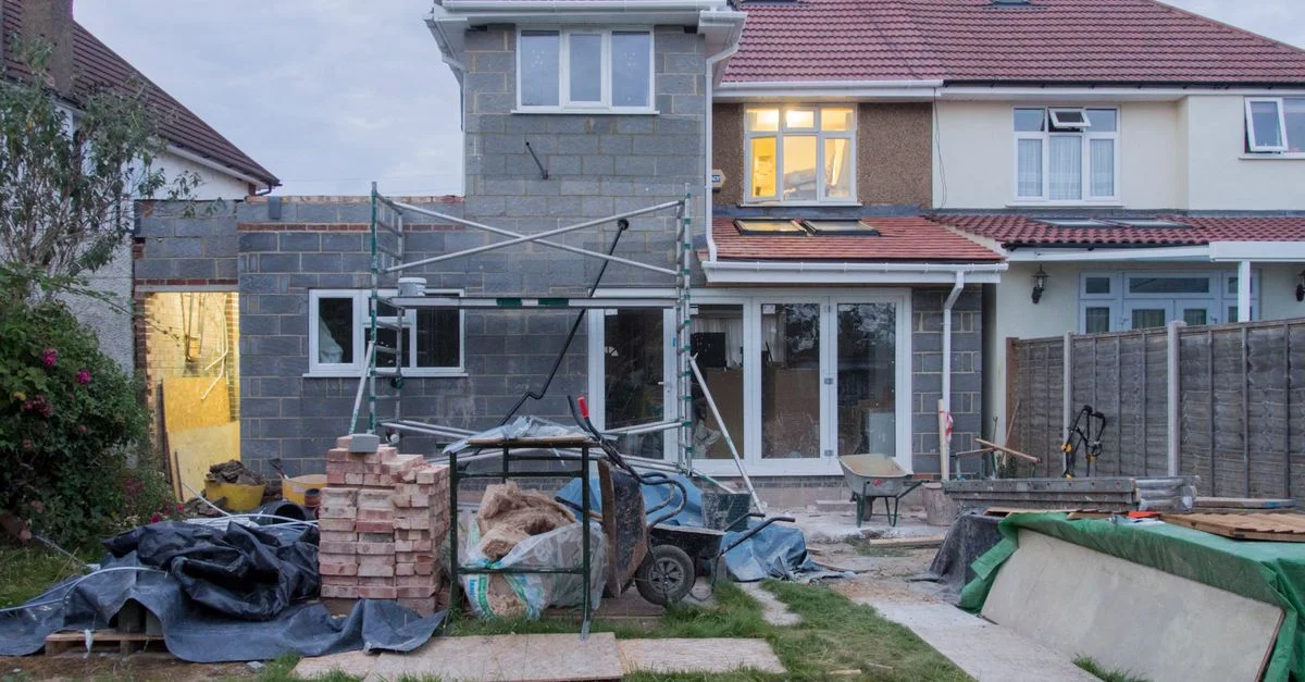 Une maison suburbaine en cours de rénovation majeure avec échafaudages et matériaux de construction.