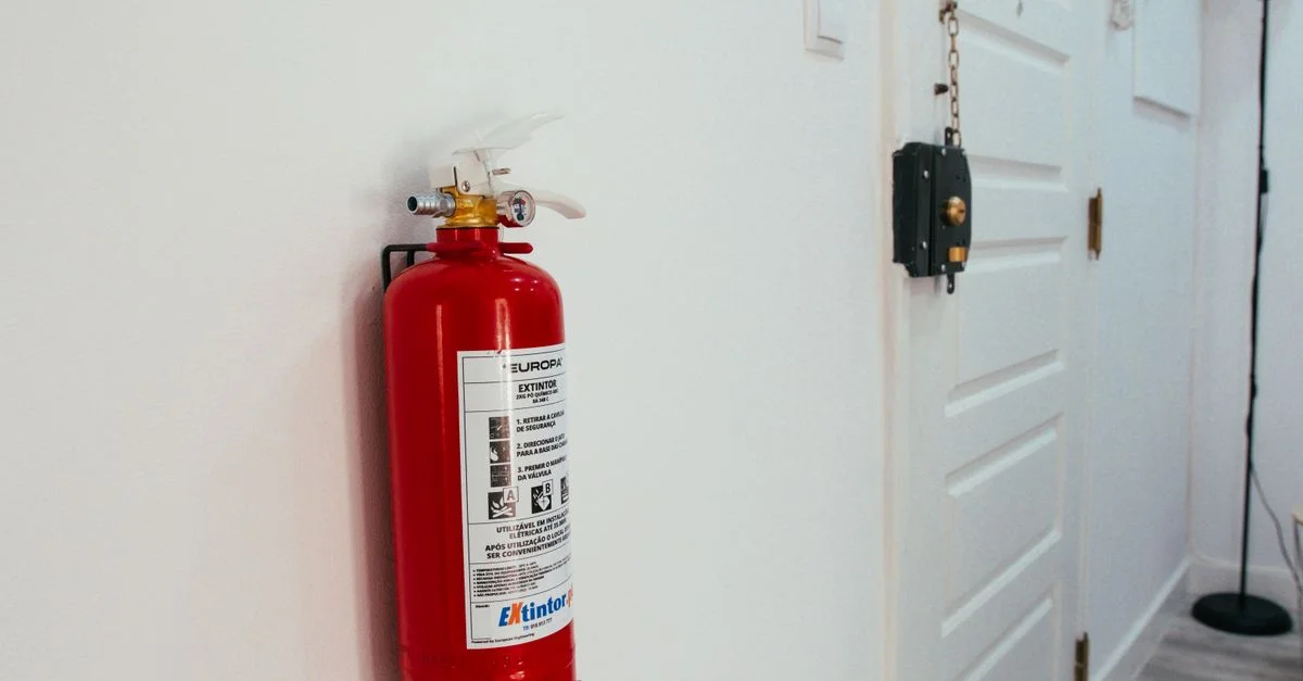 Extincteur de feu rouge monté sur un mur blanc dans un couloir d'appartement moderne.