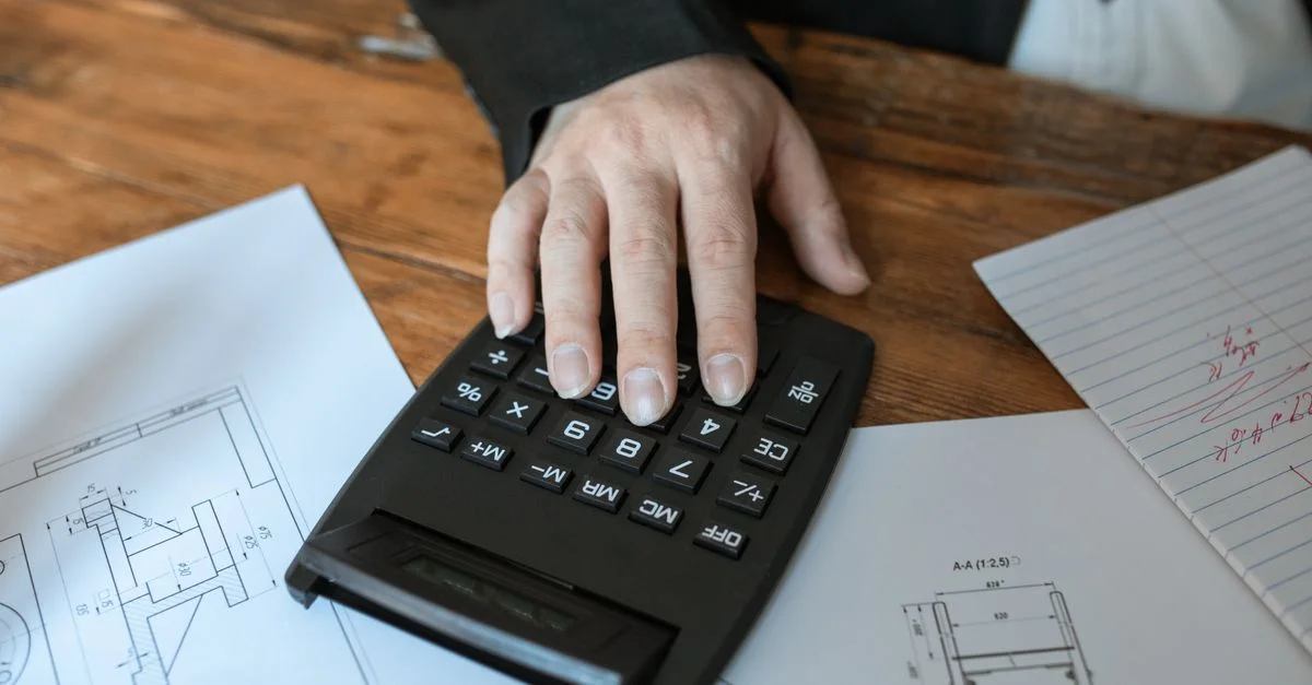 Main utilisant une calculatrice pour des calculs architecturaux sur des plans.