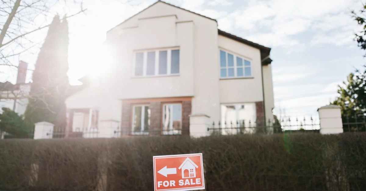 Maison lumineuse en banlieue avec une enseigne à vendre au premier plan.
