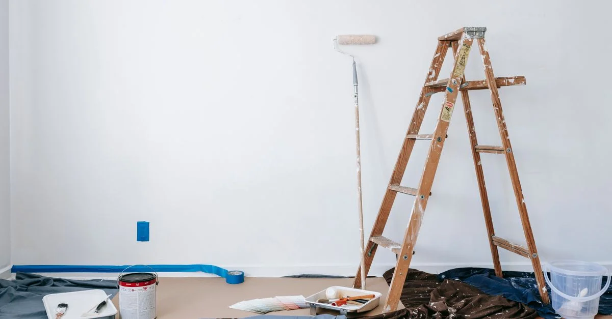 Une pièce préparée pour la rénovation avec une échelle, des fournitures de peinture et une toile de protection.
