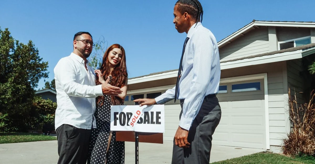 Un couple rencontre un agent immobilier pour finaliser l'achat de leur nouvelle maison, indiqué par un panneau 'Vendu'.