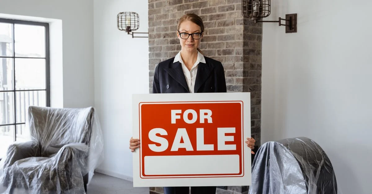 Agent immobilier tenant un panneau 'À Vendre' dans un salon meublé.