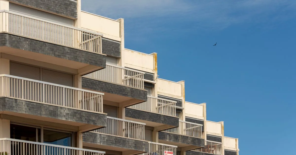 Un immeuble moderne avec de distincts balcons contre un ciel bleu clair.