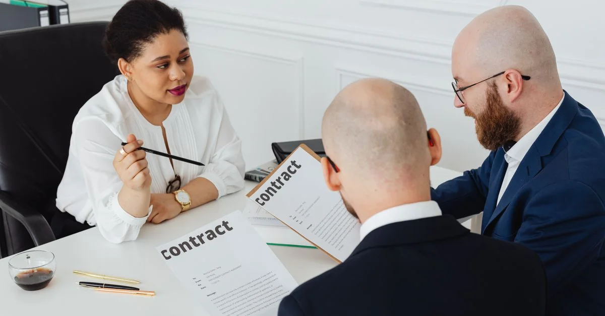 Trois professionnels discutent d'un contrat dans un bureau moderne.