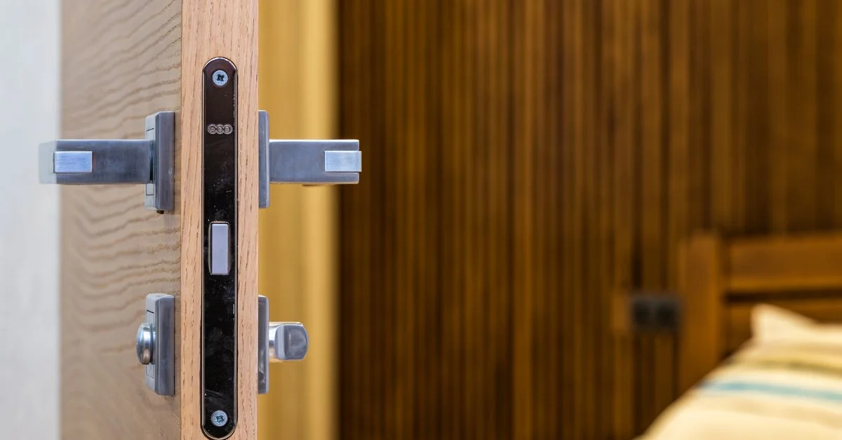 Gros plan sur une porte en bois moderne avec un verrou en métal, menant à un cadre de chambre cosy.