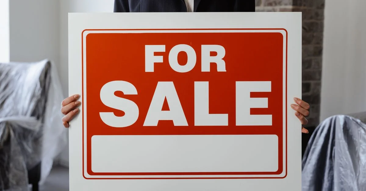 Gros plan d'une personne en costume tenant un panneau À vendre dans une pièce meublée.